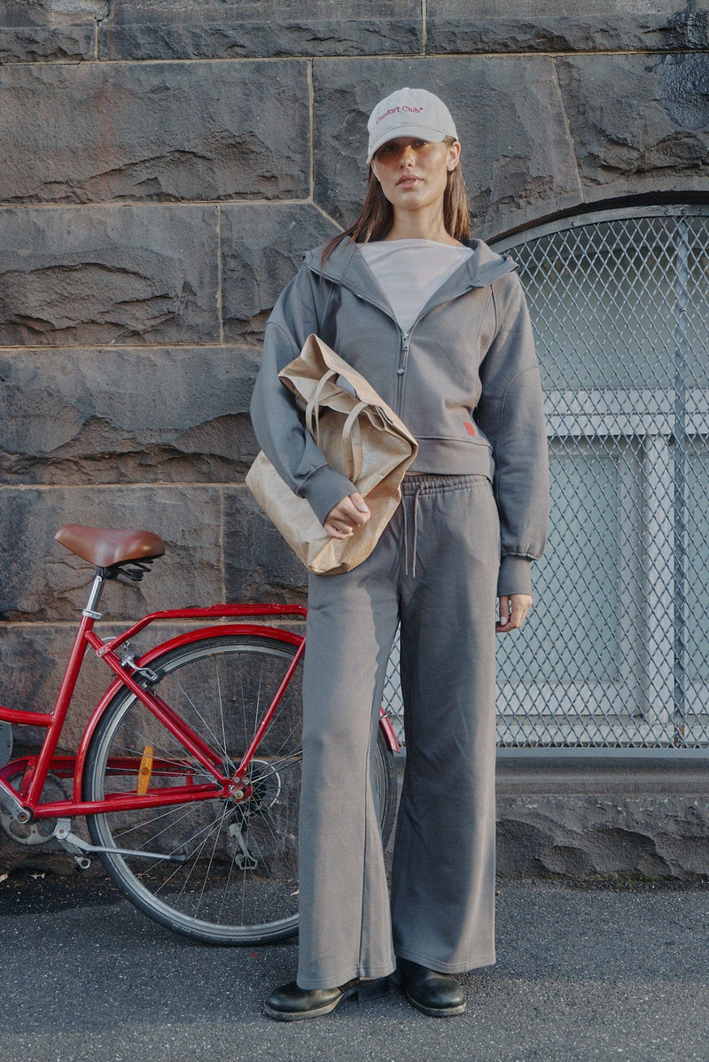 Model in grey half-zip top and relaxed pants against a bluestone wall