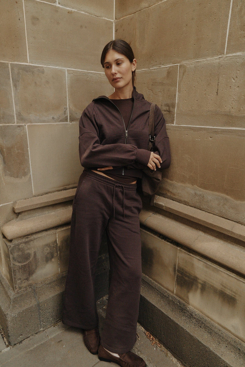 Model seated outdoors on a stone ledge in relaxed track pants